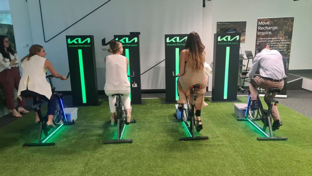 Equipo en reto KIA pedaleando bicicletas que generan electricidad sobre césped artificial