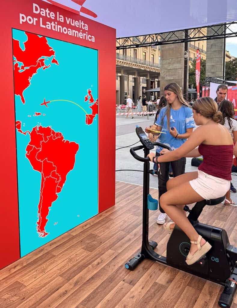 Participante pedaleando bicicleta generadora frente a pantalla interactiva con mapa de Latinoamérica